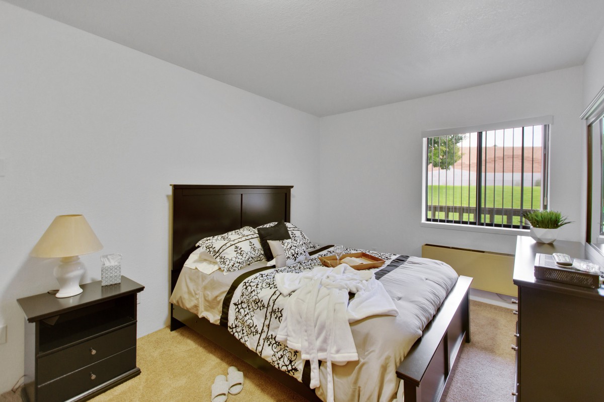 A cozy bedroom featuring a neatly made bed, nightstand, and a large window offering natural light.