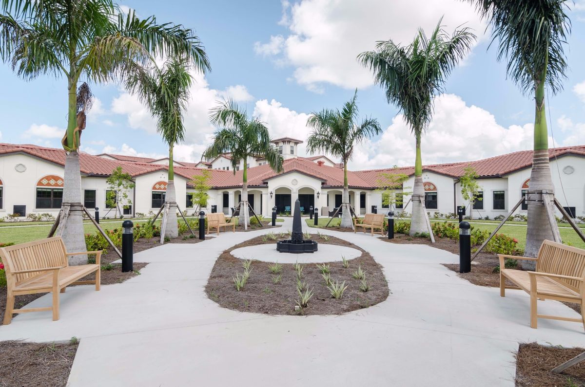 A scenic view of a building surrounded by palm trees, featuring a central pathway leading to a fountain.