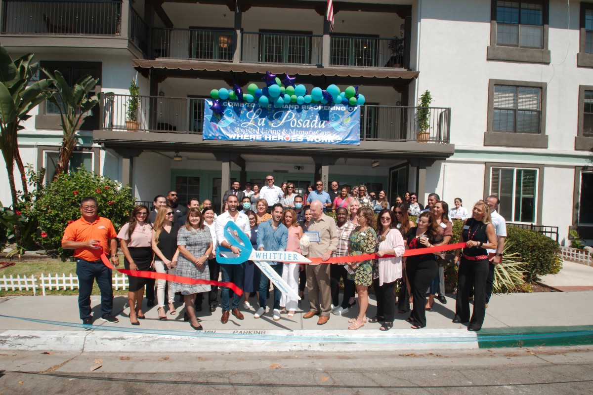 A group of people gathered for a ribbon-cutting ceremony in front of a building, decorated with balloons.