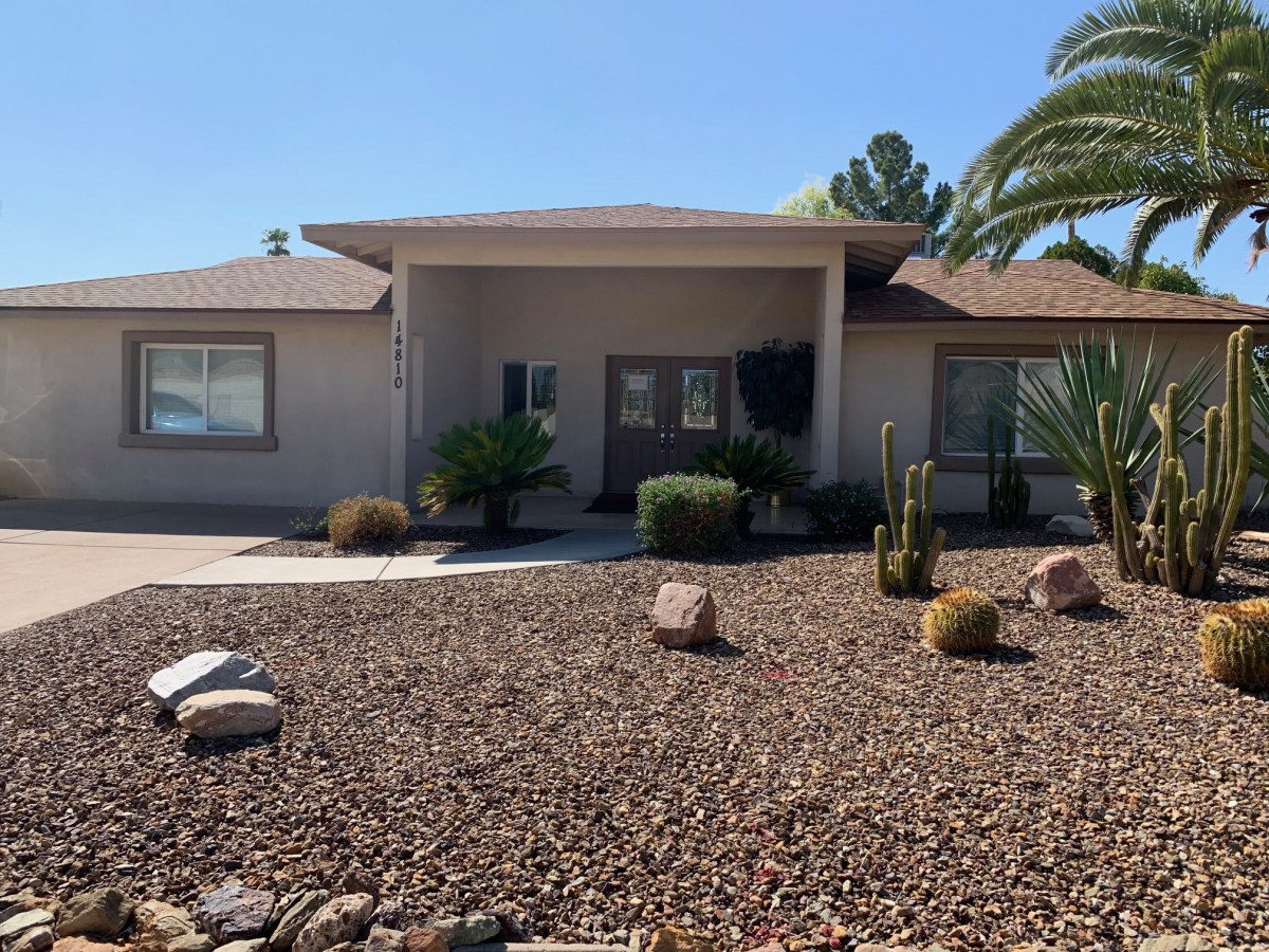 A house with a desert-inspired front yard featuring xeriscaping, cacti, and a palm tree.