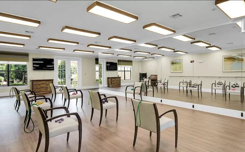 A spacious room with wooden flooring, arranged chairs, and mirrored walls under modern ceiling lights.