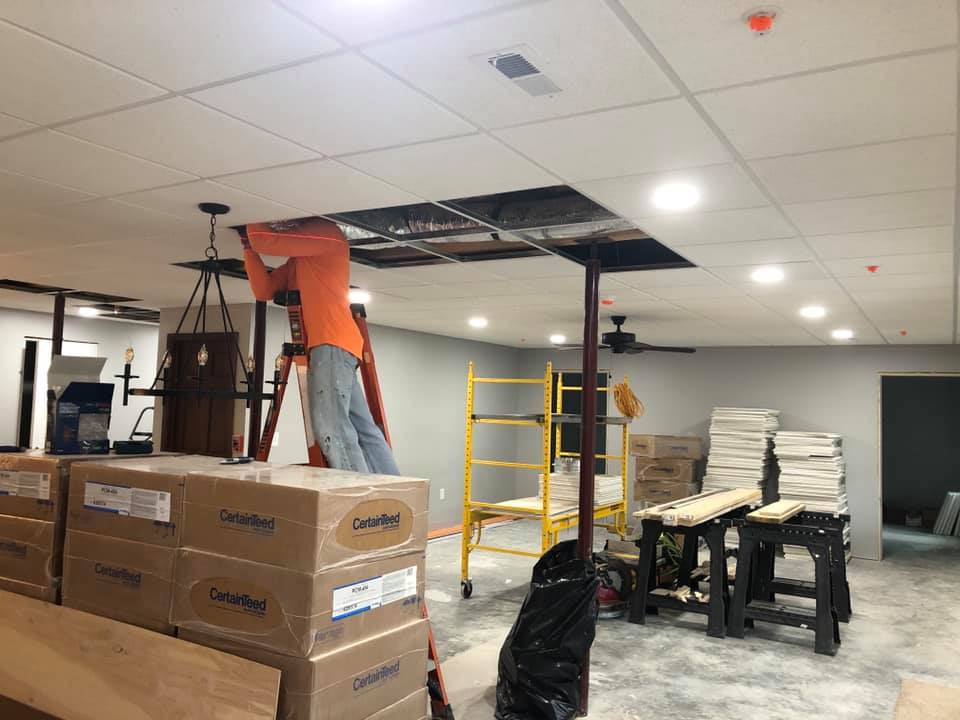 A worker is repairing the ceiling in a room filled with boxes and scaffolding.
