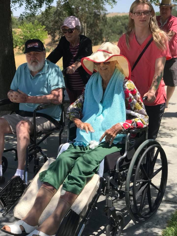 A group of people enjoying a sunny day outdoors, with two individuals seated in wheelchairs.