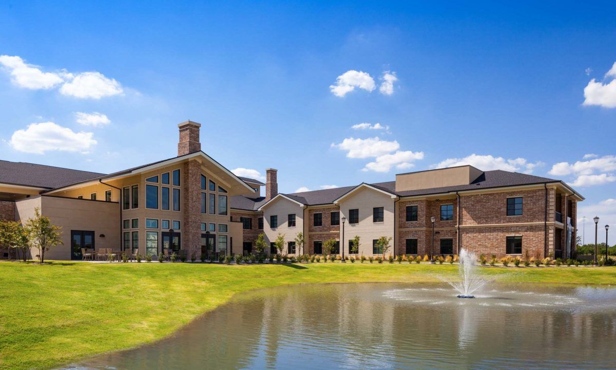 A scenic view of a modern building with a pond and fountain in the foreground.