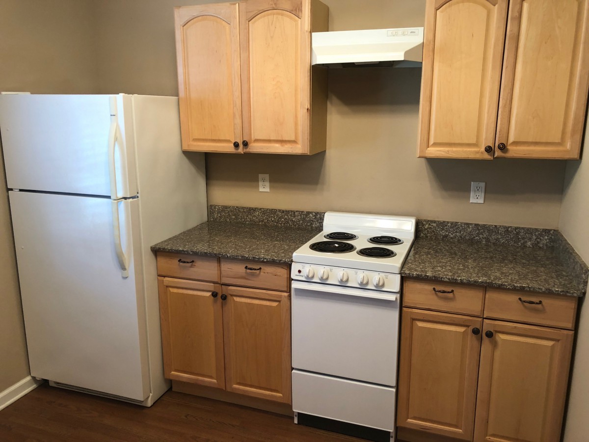 A kitchen with wooden cabinets, a white refrigerator, and a compact electric stove.