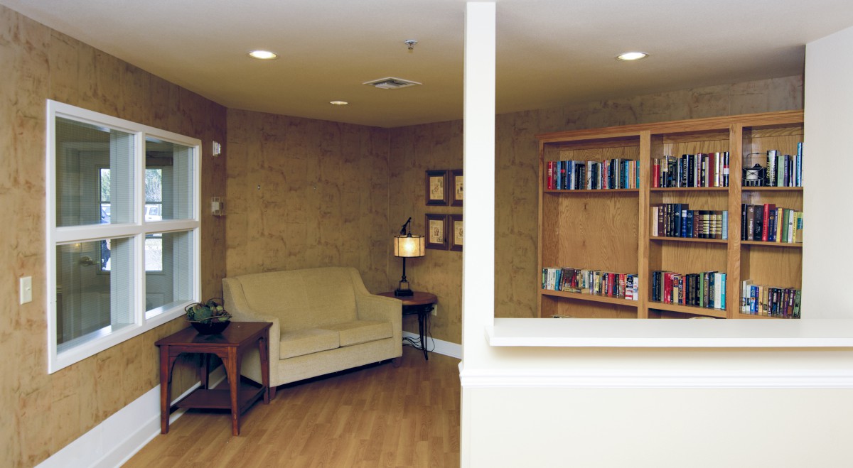A cozy living room with a beige sofa, a bookshelf filled with books, and a lamp providing ambient lighting.