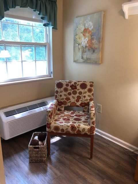 A cozy corner featuring a floral-patterned chair next to a window, with a decorative painting on the wall and a basket on the floor.