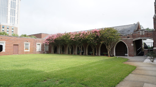 A serene courtyard featuring a beautiful building with flowering trees and a well-maintained lawn.