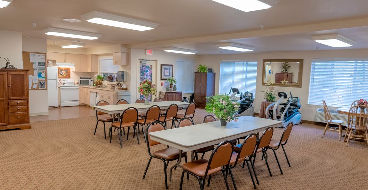 A bright and welcoming community dining area with neatly arranged tables and chairs, decorated with indoor plants.