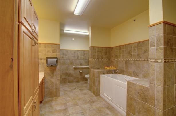 A spacious, accessible bathroom features tiled walls and floor, a bathtub with handrails, and modern fixtures.