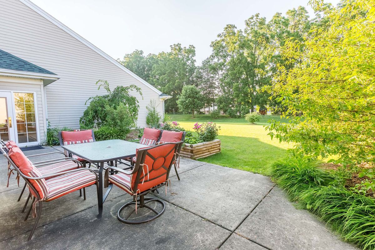 A sunny backyard patio with a dining set and lush green garden.