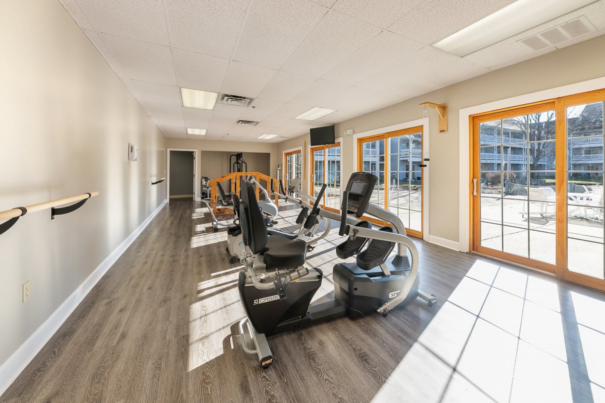 A well-lit gym featuring various exercise machines, including treadmills and elliptical trainers.