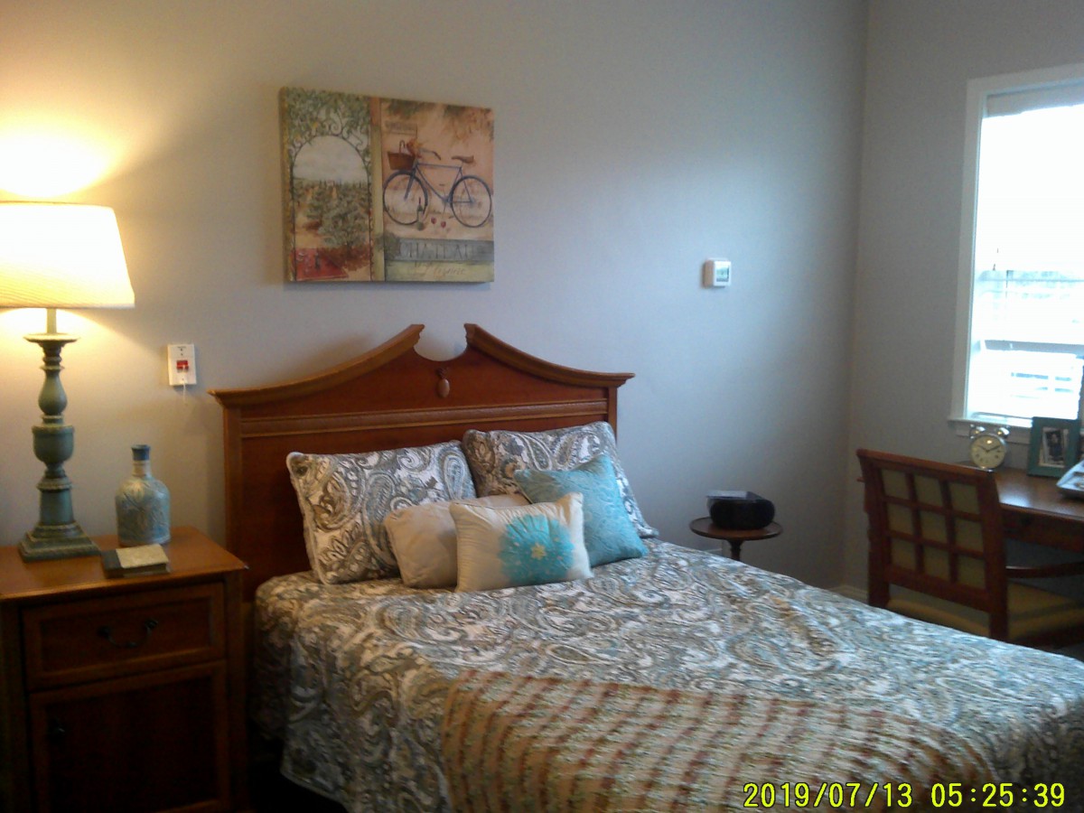 A cozy bedroom with a patterned bedspread, decorative pillows, and wall art.