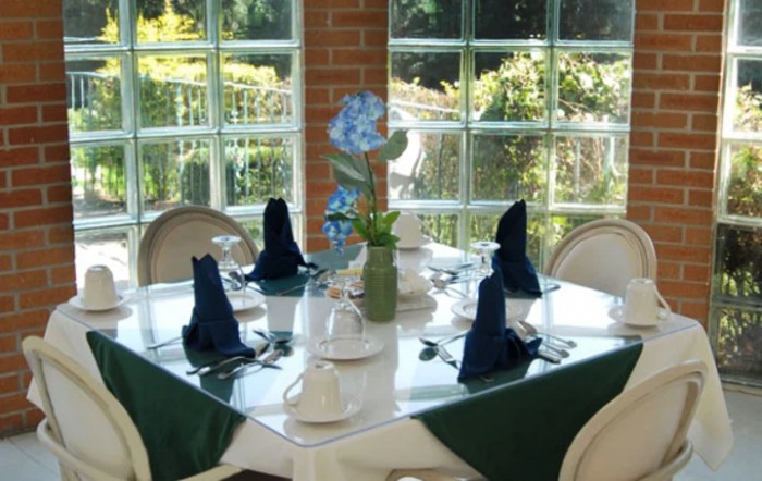 A neatly set dining table with blue napkins and a floral centerpiece in a bright, windowed restaurant area.