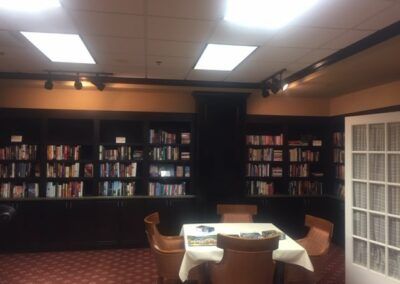 A cozy library reading room with bookshelves and a table surrounded by chairs.