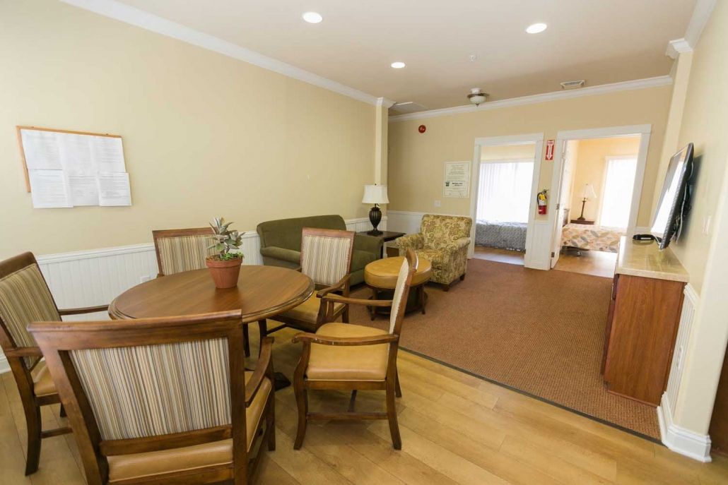 A cozy living room with a dining area, featuring a round wooden table surrounded by chairs, a comfortable sofa, and a lamp.