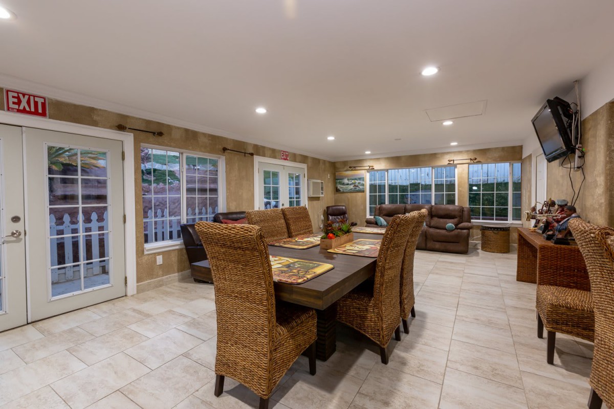 A spacious dining room with wicker chairs and a rectangular table, surrounded by large windows.