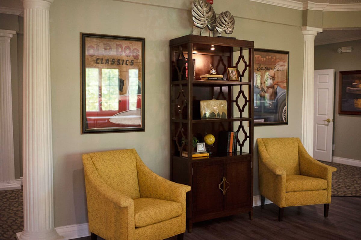 A cozy living room with yellow chairs, a bookshelf adorned with decorative items, and framed posters on the wall.