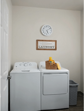A laundry room featuring a washing machine, dryer, wall clock, and decorative sign.