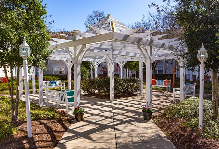 A sunlit pergola with outdoor seating in a garden setting.