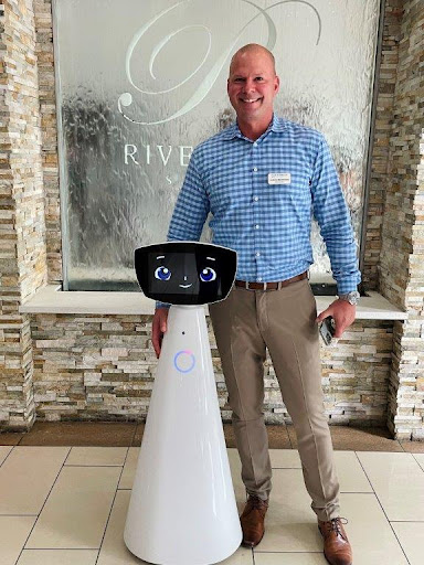 A man standing next to a friendly-looking robot in a modern lobby.