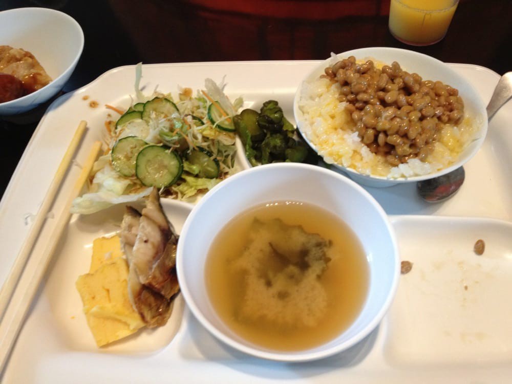A traditional Japanese breakfast featuring miso soup, natto with rice, salad, and tamagoyaki.