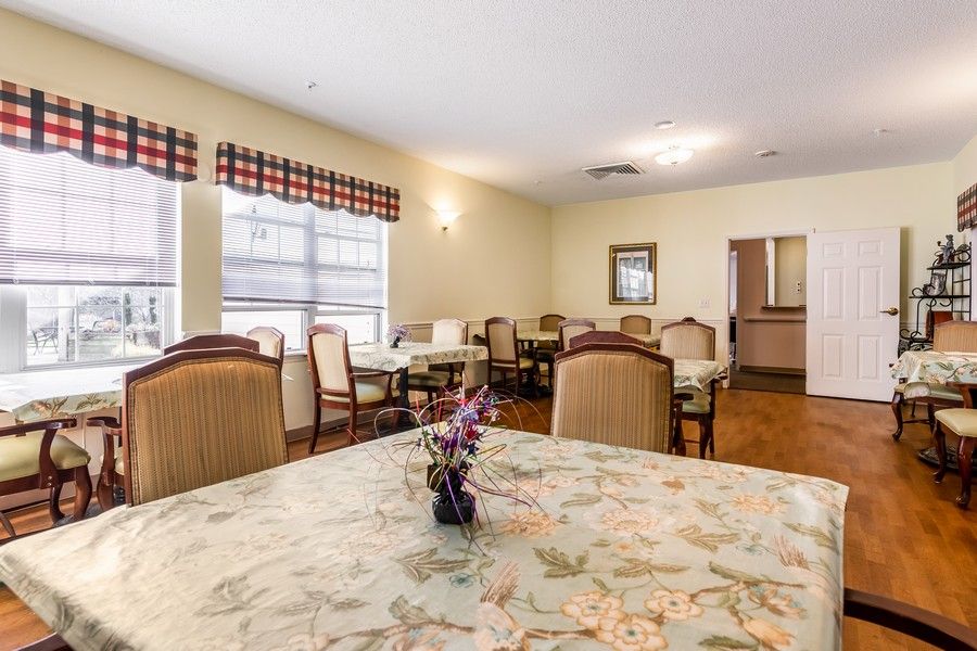 A cozy dining room with multiple tables and chairs, decorated with floral patterns and natural light from the window.