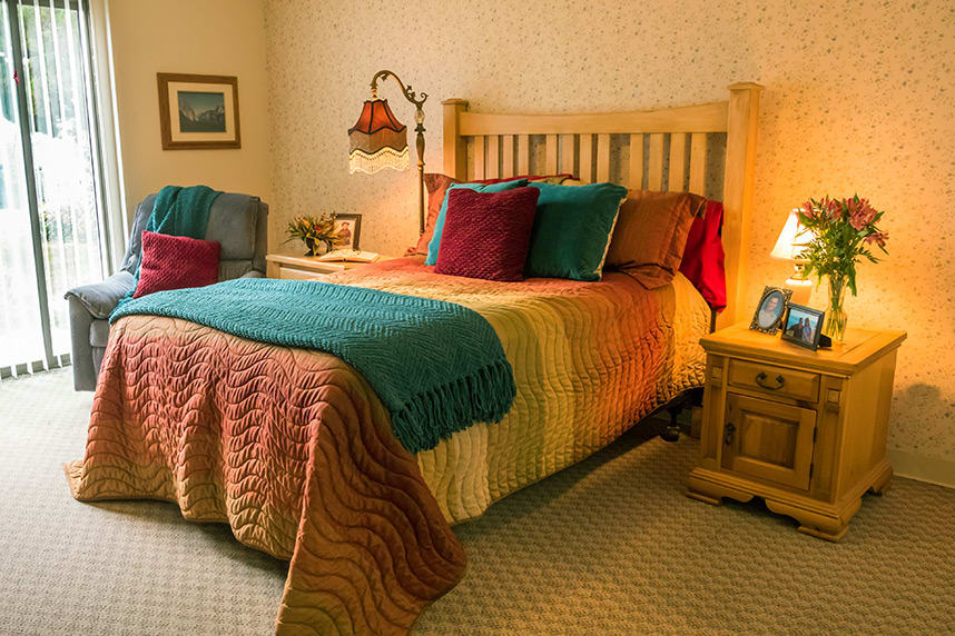 A cozy bedroom with a colorful quilt, decorative pillows, and warm lighting.