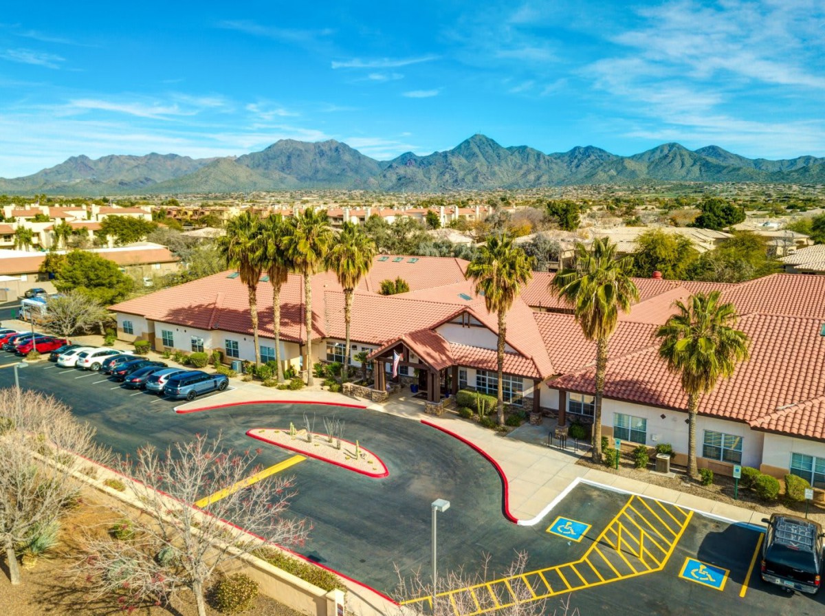 Aerial view of a building surrounded by palm trees with mountains in the background.