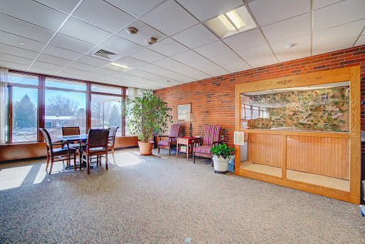 A spacious office interior featuring a meeting area with large windows, comfortable seating, and decorative plants.