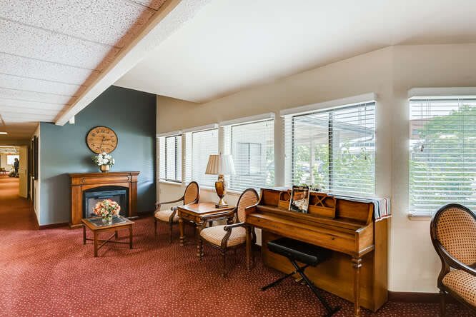 A cozy living room with a piano, chairs, and a fireplace by the window.