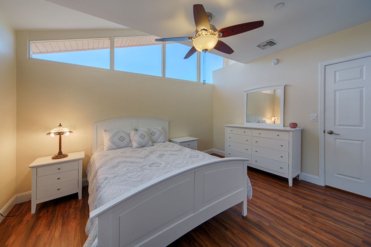 A cozy bedroom featuring a white bed and dresser, with a ceiling fan and wooden flooring.
