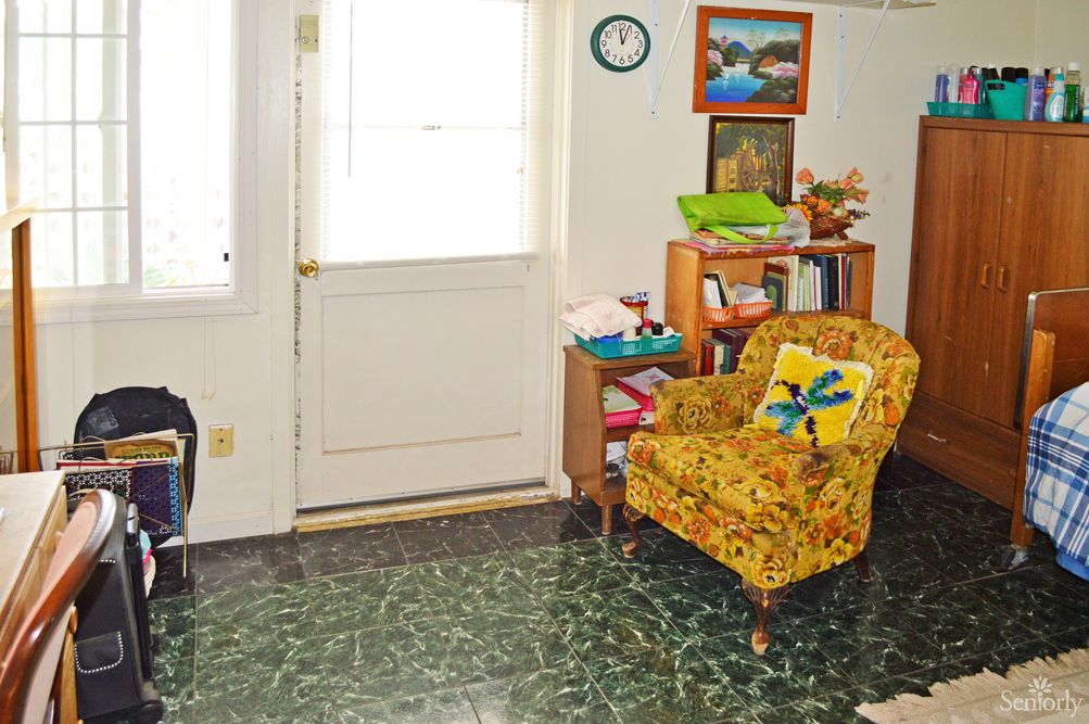 A cozy living room with a vintage yellow chair, bookshelf, and artwork on the walls.