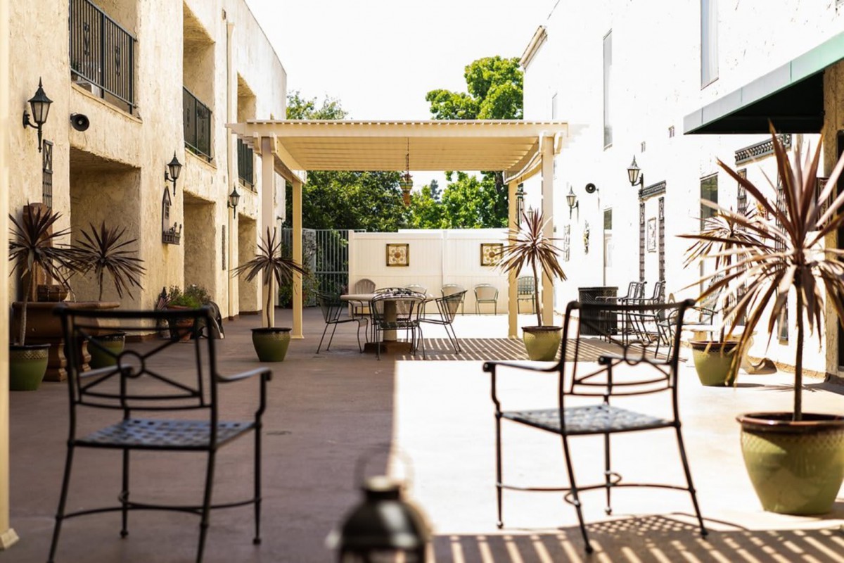 A sunny outdoor patio area with tables, chairs, and a pergola providing some shade.