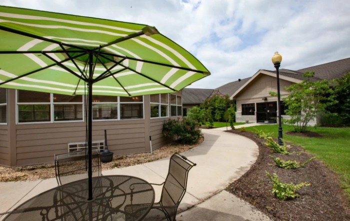 A patio area with a striped green umbrella, outdoor furniture, and a curving pathway leading to a building.