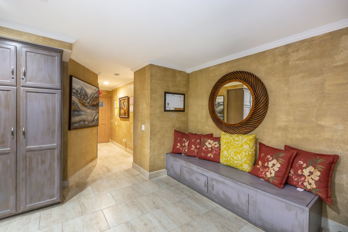 A cozy hallway interior featuring a framed mirror, cushioned seating with colorful pillows, and decorative wall art.