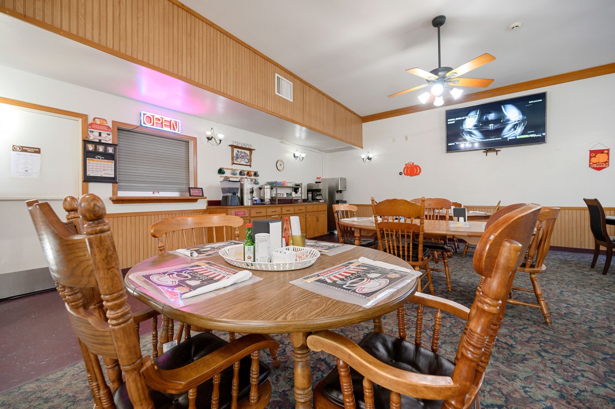 A cozy restaurant dining area featuring wooden tables and chairs, with a television mounted on the wall.