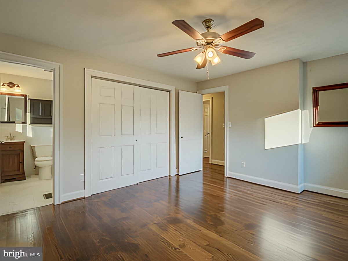 An empty room with hardwood flooring, a ceiling fan, a closet with sliding doors, and a window.