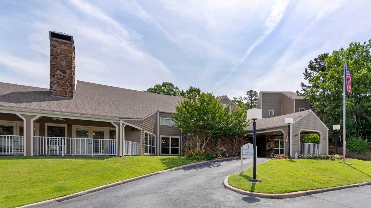 The image shows a building with a driveway and surrounding greenery under a clear sky.