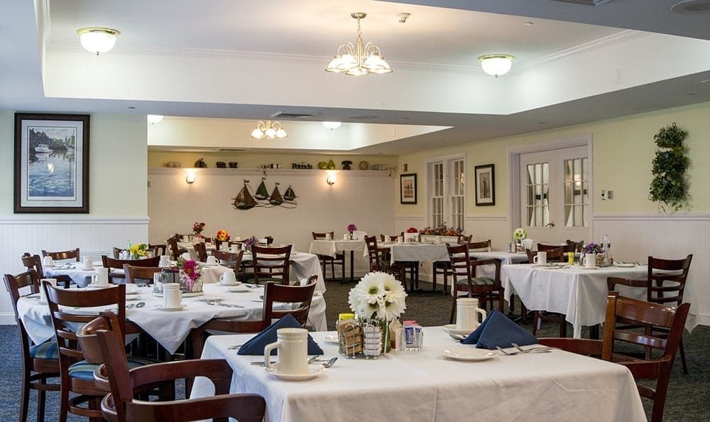 A neatly arranged dining area with tables set for guests, featuring floral centerpieces and tasteful wall decorations.
