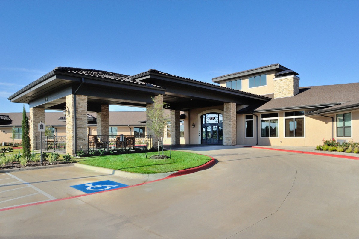 A modern building entrance with a covered driveway and parking area, under a clear blue sky.