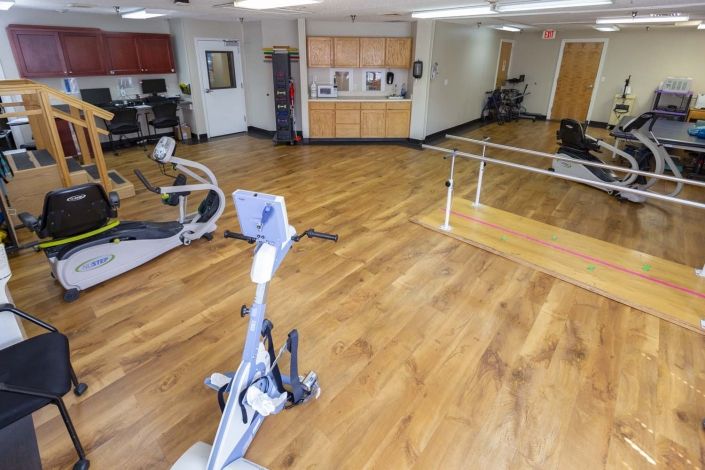 A spacious rehabilitation room with exercise equipment and wooden flooring.