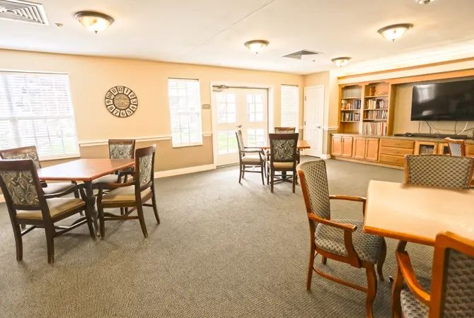 A spacious and well-lit room with tables, chairs, and a bookshelf.