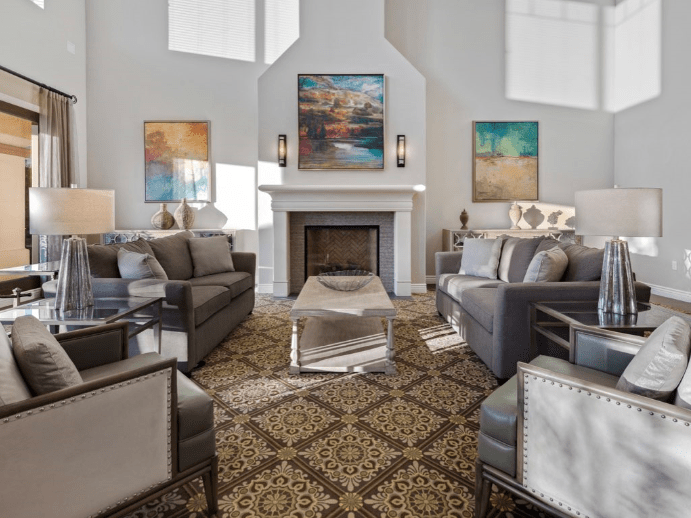 A modern and elegantly designed living room featuring a stylish sofa set, a central fireplace, colorful artwork on the walls, and a decorative patterned rug.