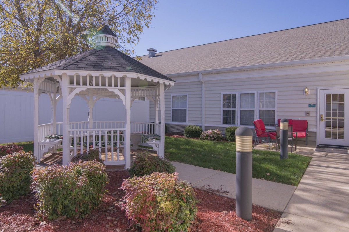 A cozy outdoor gazebo surrounded by garden landscaping next to a building.