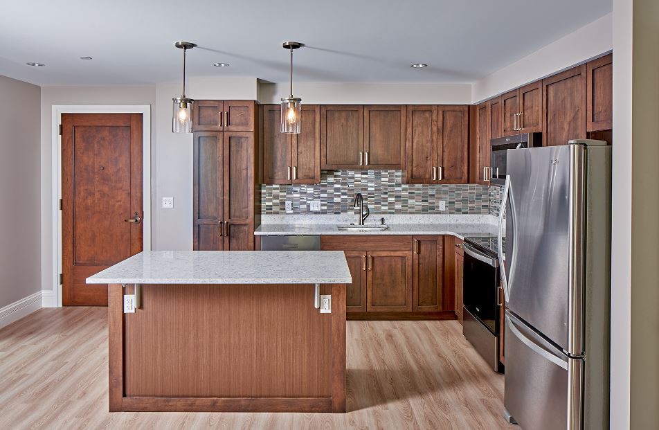 A modern kitchen with wooden cabinets, featuring an island and stainless steel appliances.