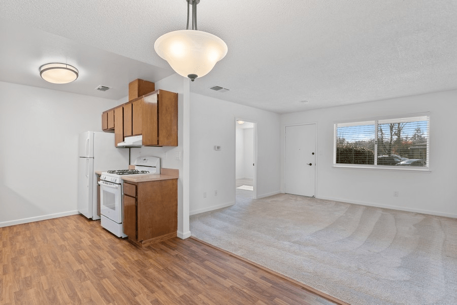 A small apartment kitchen with wooden cabinets and a light fixture, featuring both wood and carpeted flooring.