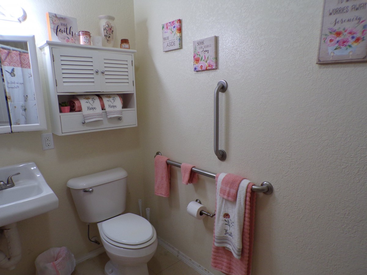 A neatly decorated bathroom with pink accents, featuring a toilet, wall-mounted shelves, towels, and wall art.