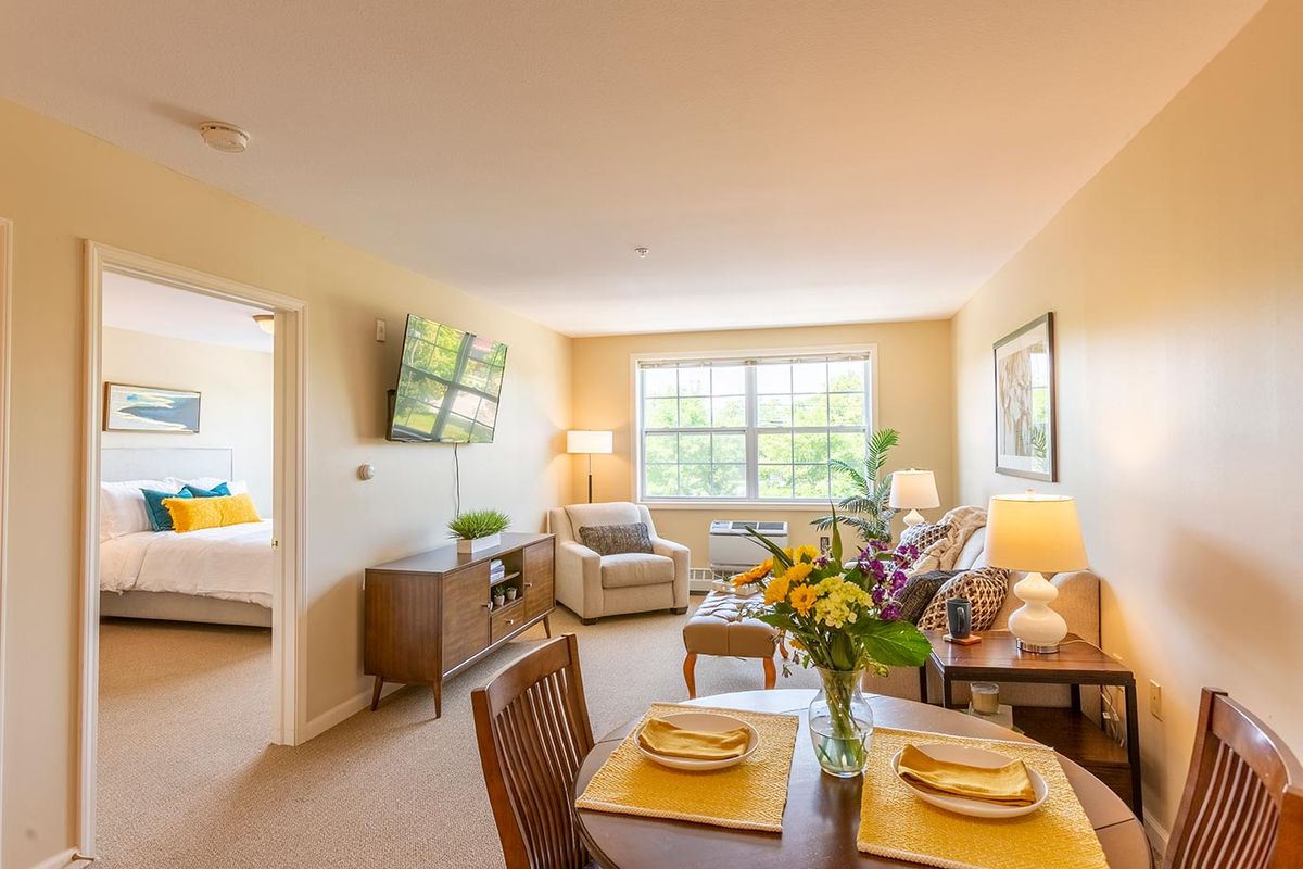 A cozy living room with a dining area, featuring a comfortable sofa, television, and a window allowing natural light.
