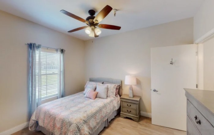 A cozy bedroom featuring a bed with patterned bedding, a nightstand with a lamp, and a ceiling fan.